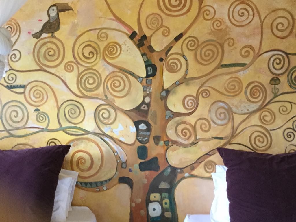 Klimt-inspired Tree of Life mural painted above bed with purple pillows